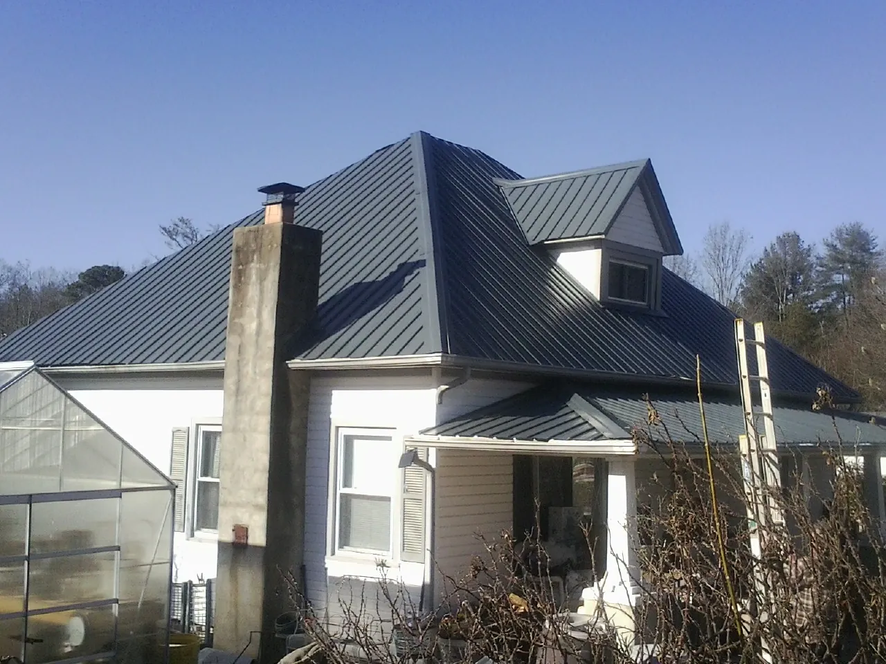 Dark blue standing seam metal roof on a white farmhouse with dormer — Slate & Tile Roof Repair by Roofing Brothers in Newaygo