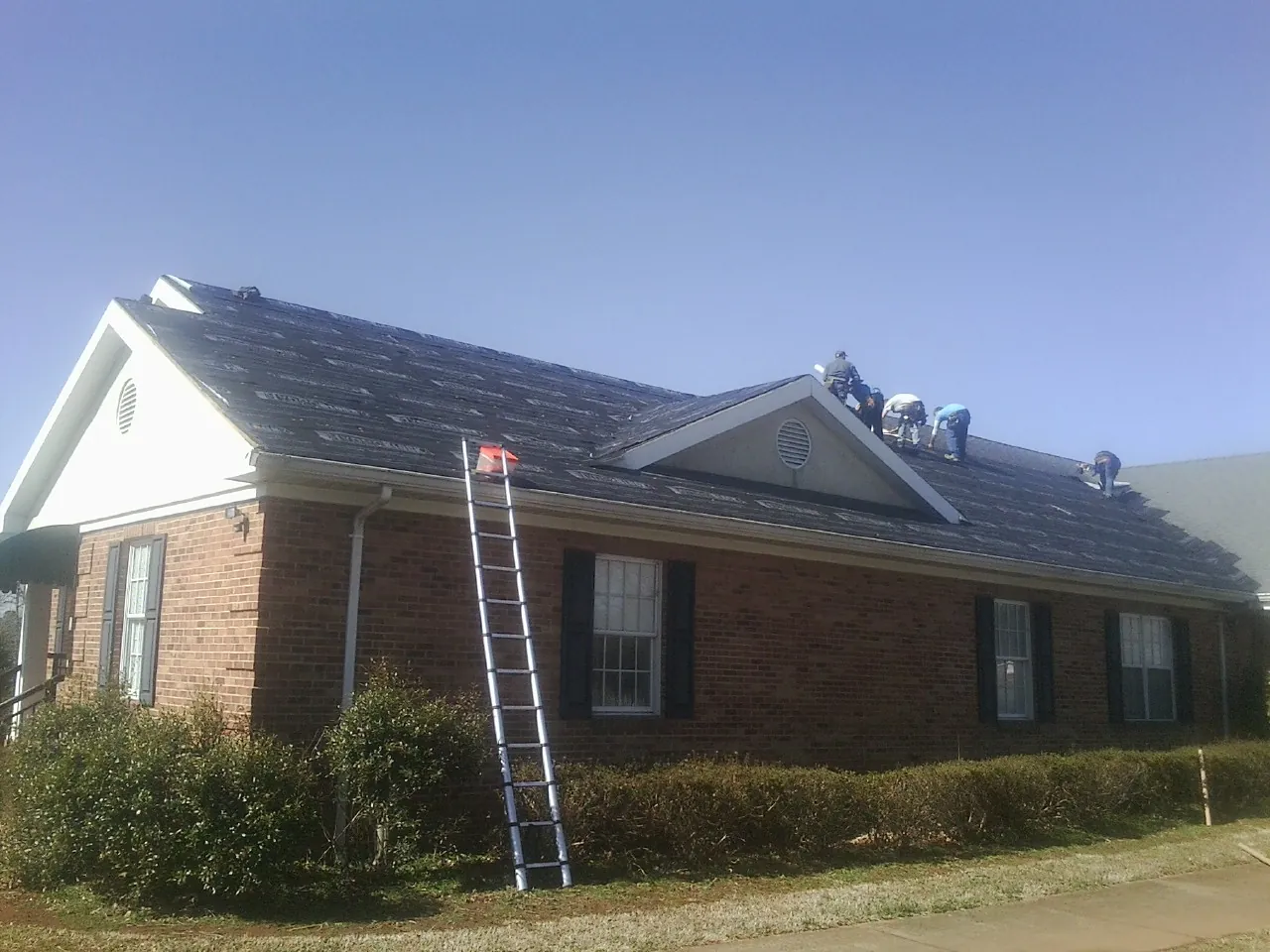 Crew tearing shingles off a brick ranch roof with a ladder set — Metal Roof Repair work by our crew in Newaygo