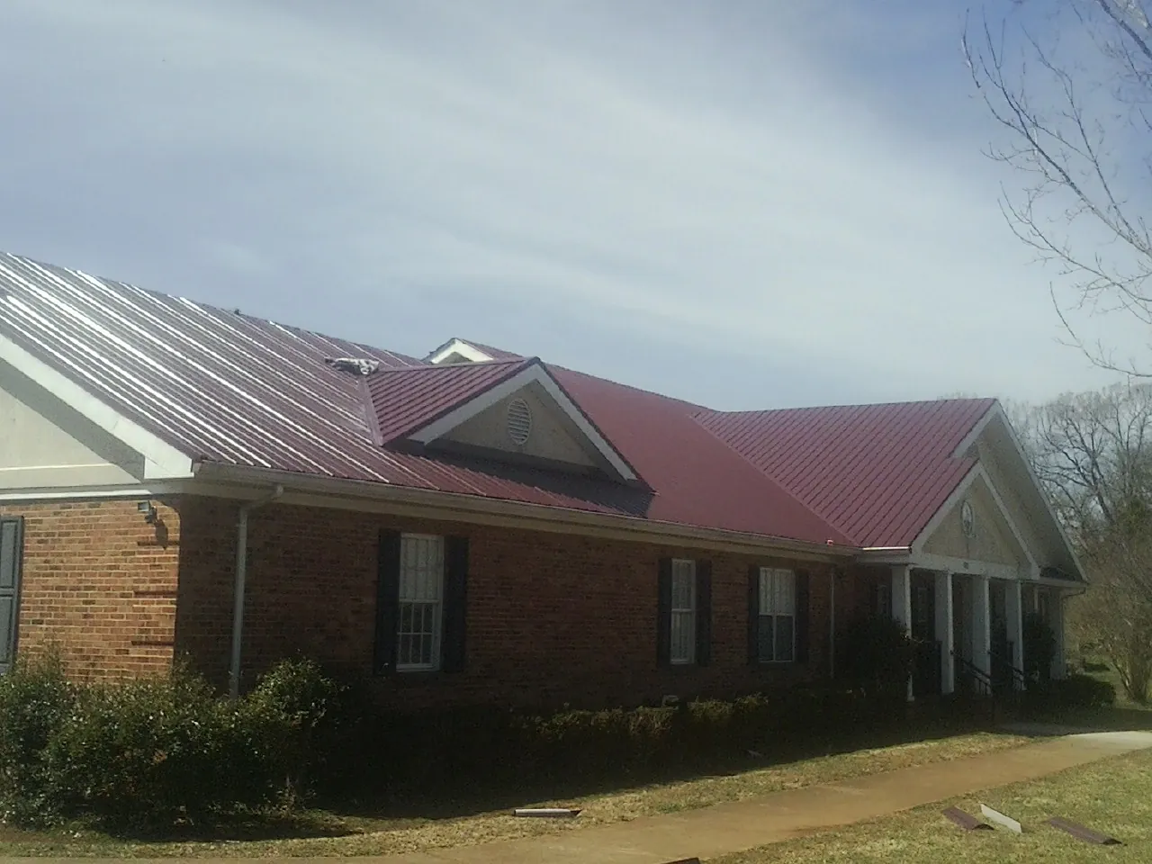 Red metal roof with gabled entries on a long brick building, from a Hail Damage Roof Repair job in Newaygo