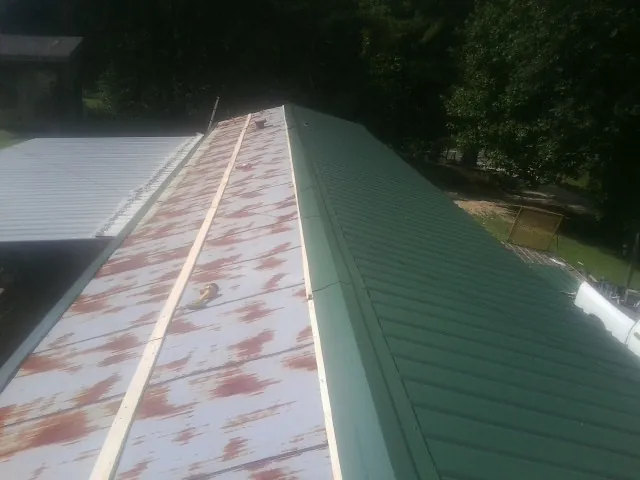 Old rusted panels beside newly installed green metal roofing — Wind Damage Roof Repair by Roofing Brothers in Newaygo