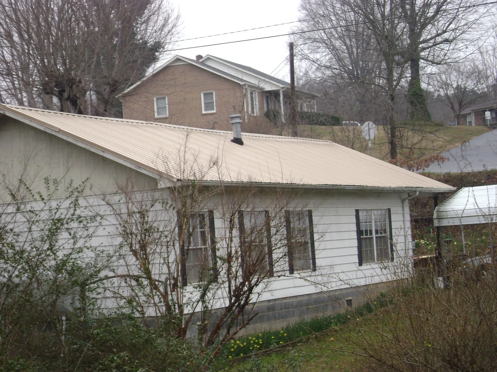 Tan metal roof on a white sided house set into a hillside — Commercial Roofing by Roofing Brothers in Newaygo