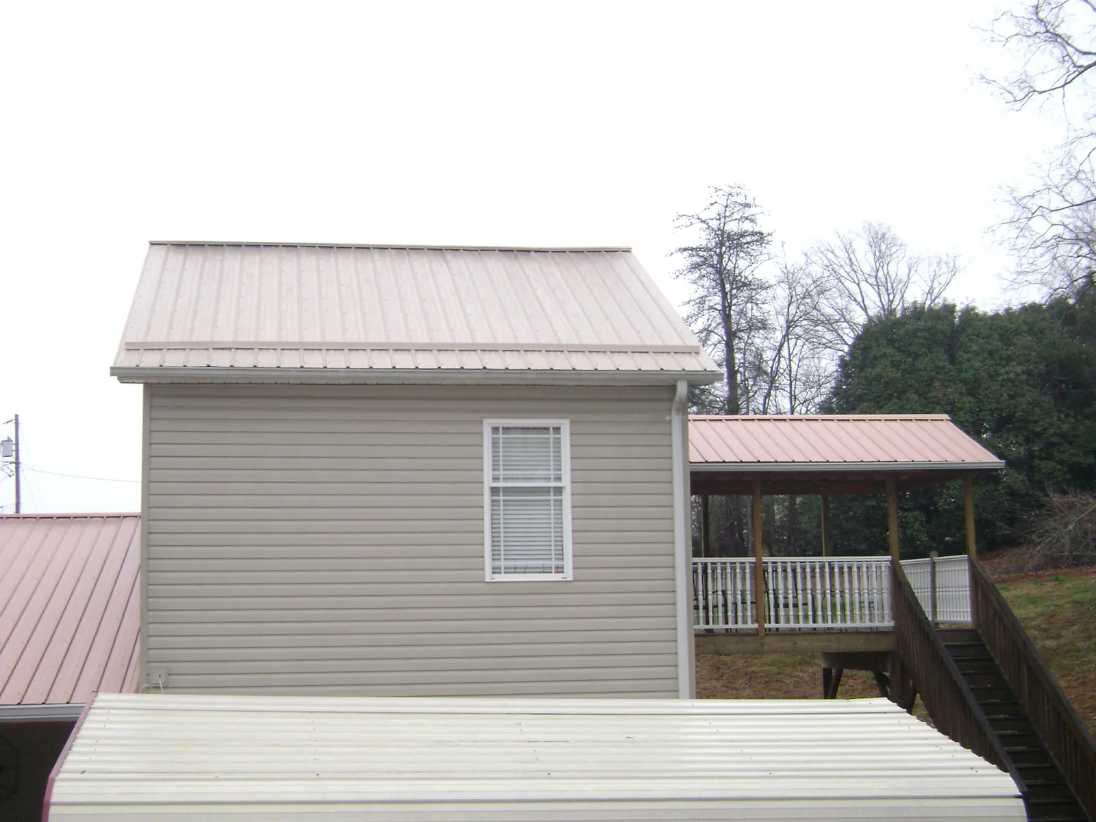Tan metal roofs on a two story addition and attached porch, from a Roof Replacement job in Newaygo