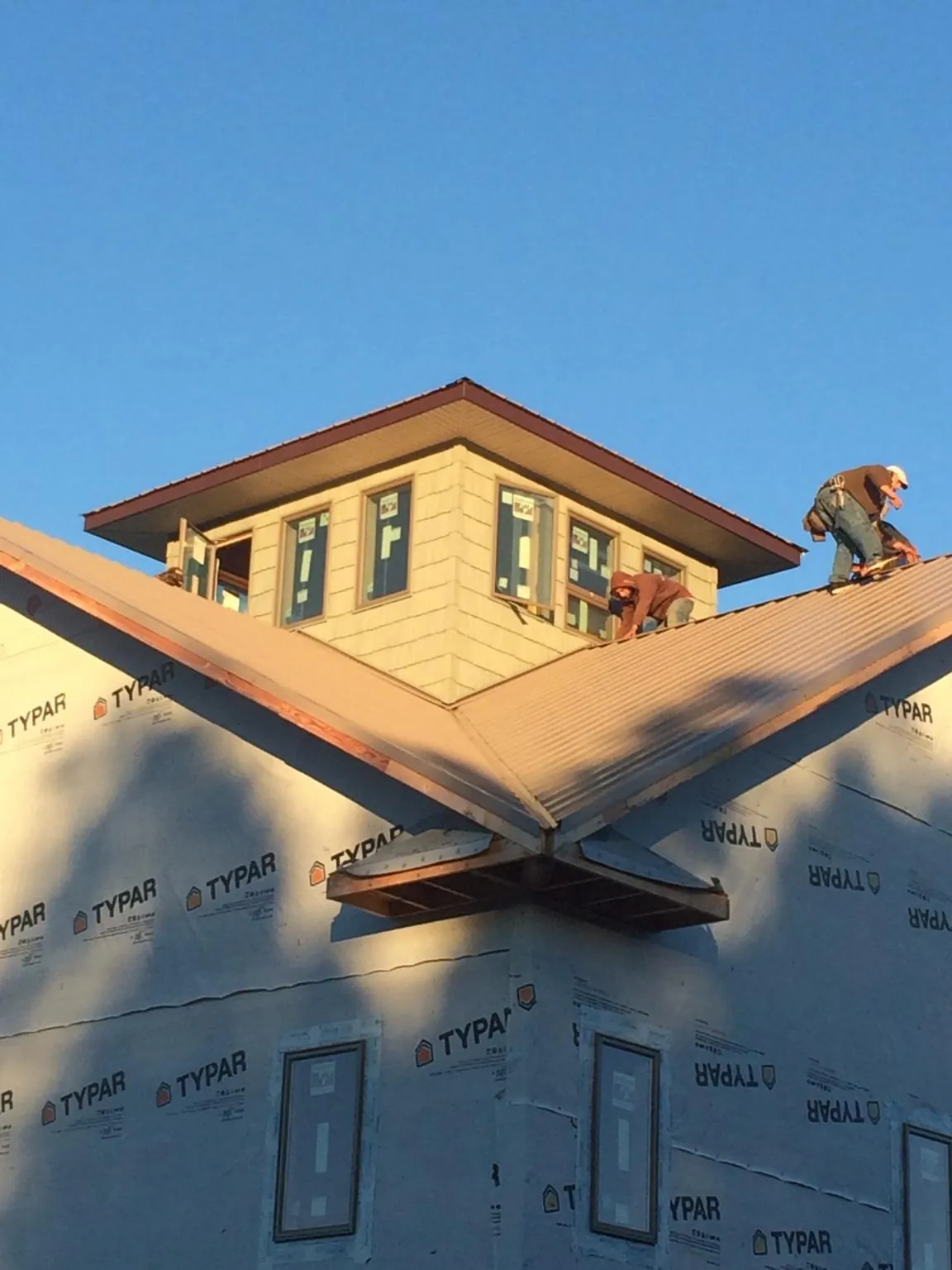 Roofers working around a rooftop cupola on a new metal roof at sunset — Roof Waterproofing in Newaygo by Roofing Brothers